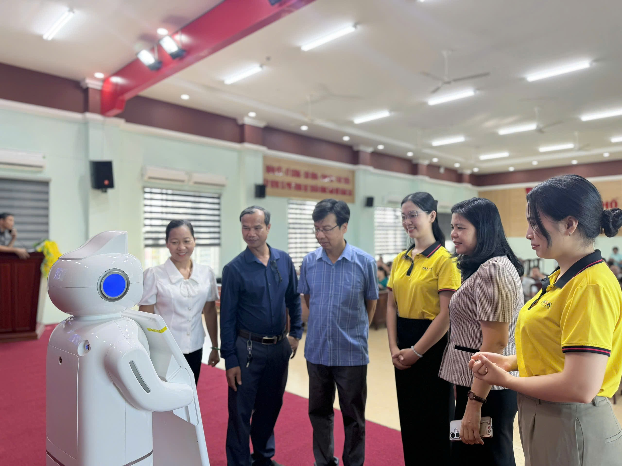 '''A group of people standing around a robot

Description automatically generated'''